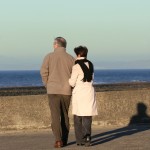 An elderly couple walikng together on a seaside promenade.