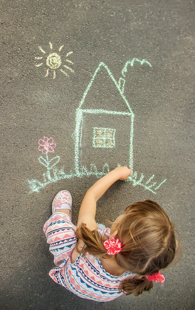 The child draws the house with chalk on the asphalt. Selective focus.